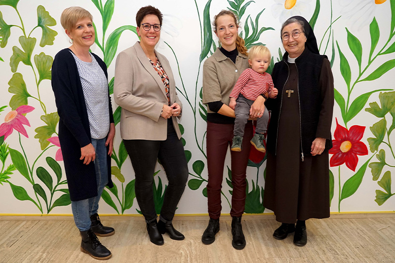 Das große Wandgemälde im Eingangsbereich ist schon fertig. Auf die Eröffnung des Kinderhauses „Kleine Freunde“ im Januar freuen sich (v.l.): Diana Ahlers, Elke Michaelis, Marlen Karthaus, hier mit Kind, und Schwester M. Angela Benoit. Foto: Michael Bodin / fcjm-presse